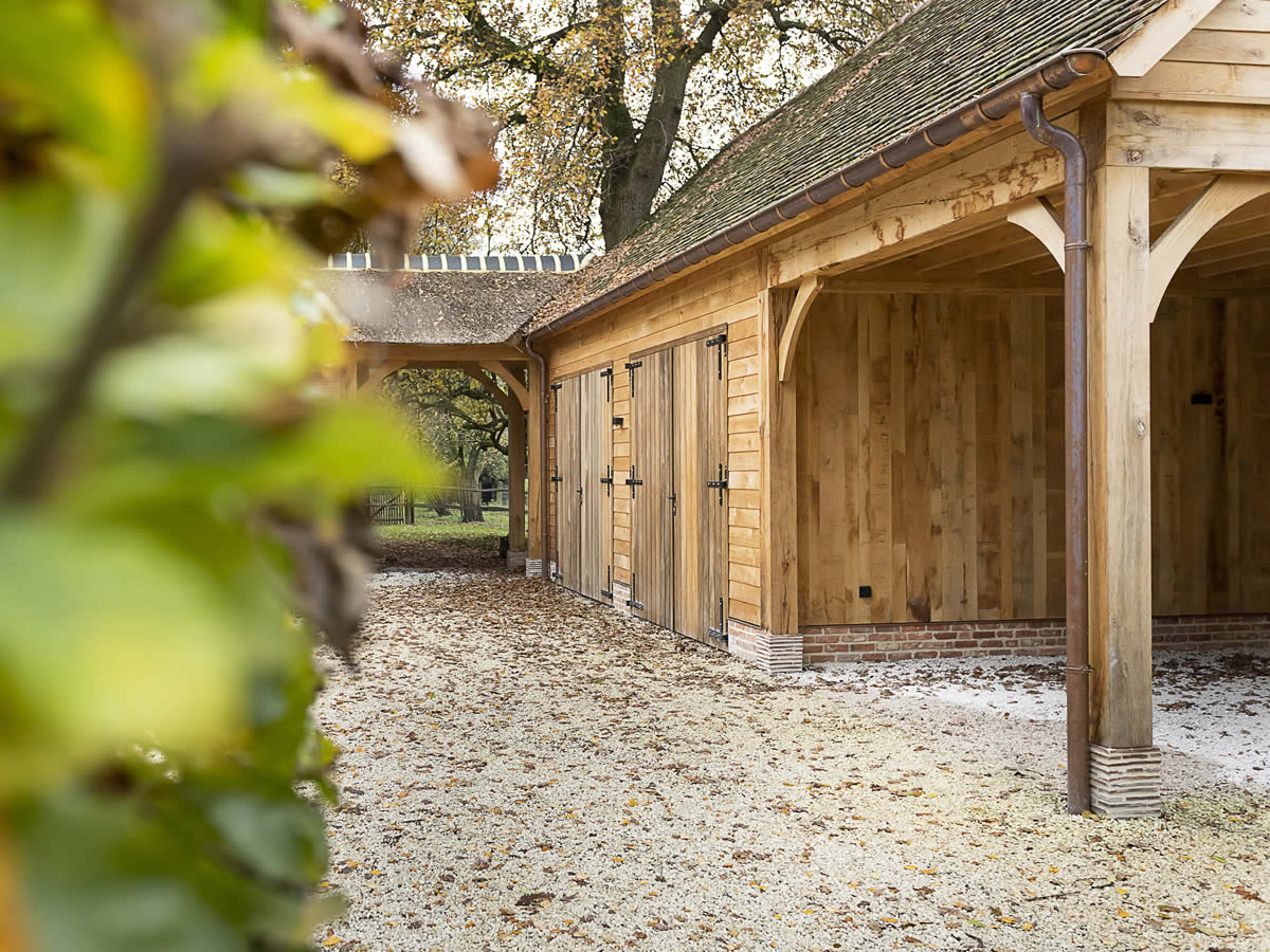 Eiken bijgebouw met dubbele poorten in padoek en rieten dak ontworpen en gebouwd door houtbouw De Meyer in Evergem. 